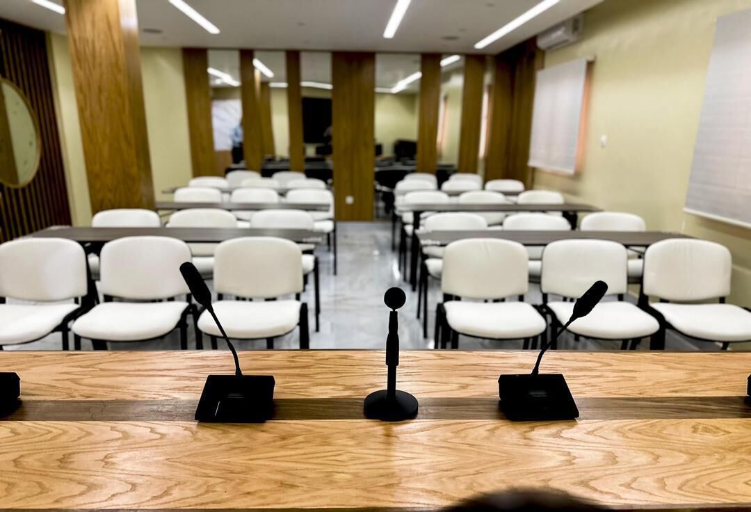 A conference room with rows of white chairs and a long table with microphones.
