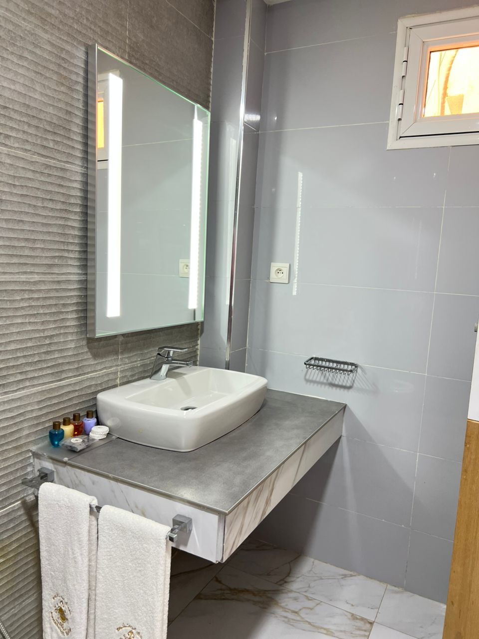 A modern bathroom with a large mirror, a white sink, and a towel rack.