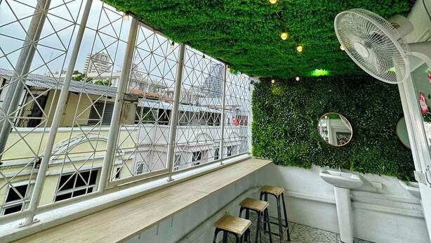 A rooftop bar with a green artificial ceiling, white bar stools, and a large fan. - Comfy Crib Hostel 2  (Bangkok)
