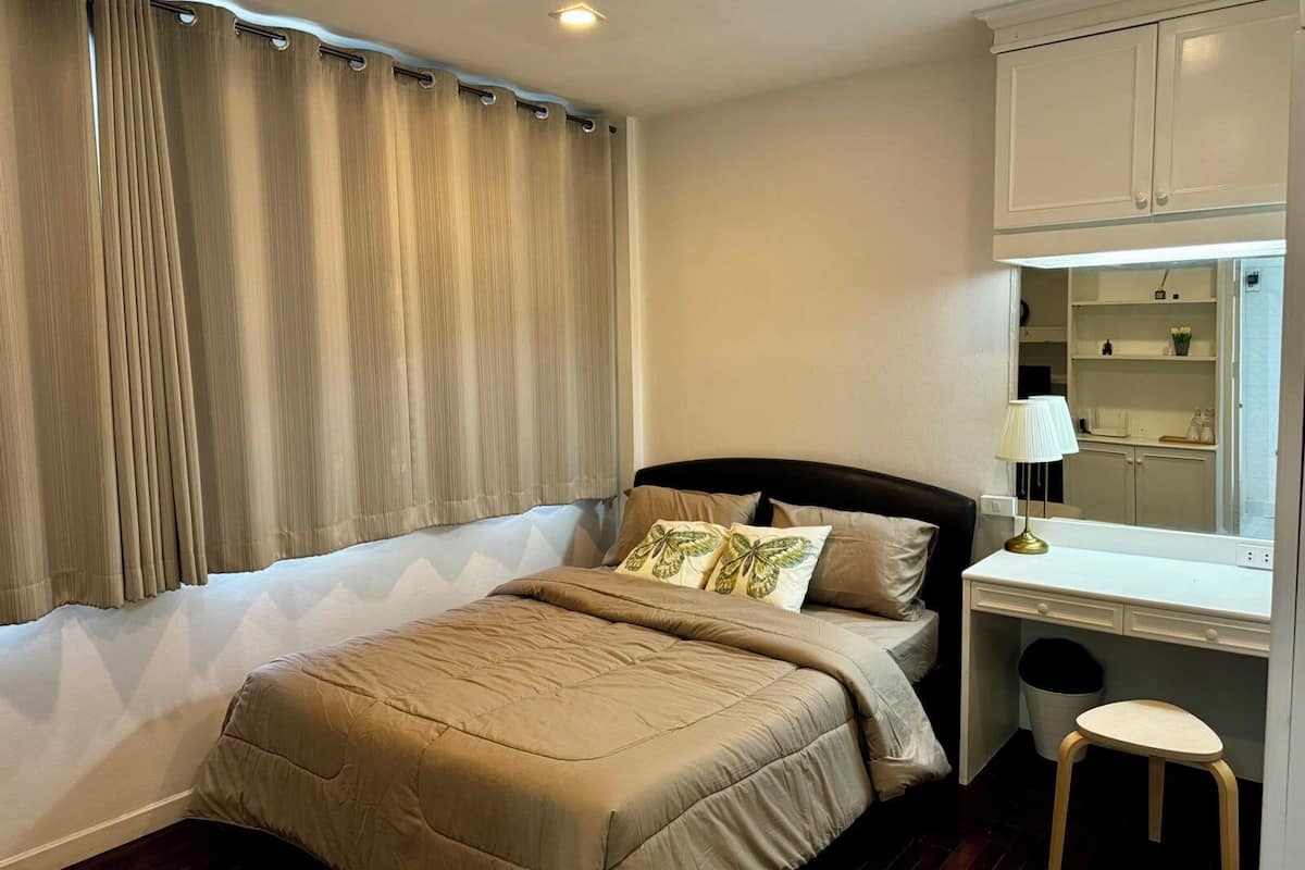 Un dormitorio con cama, escritorio, silla y ventana con cortinas.
