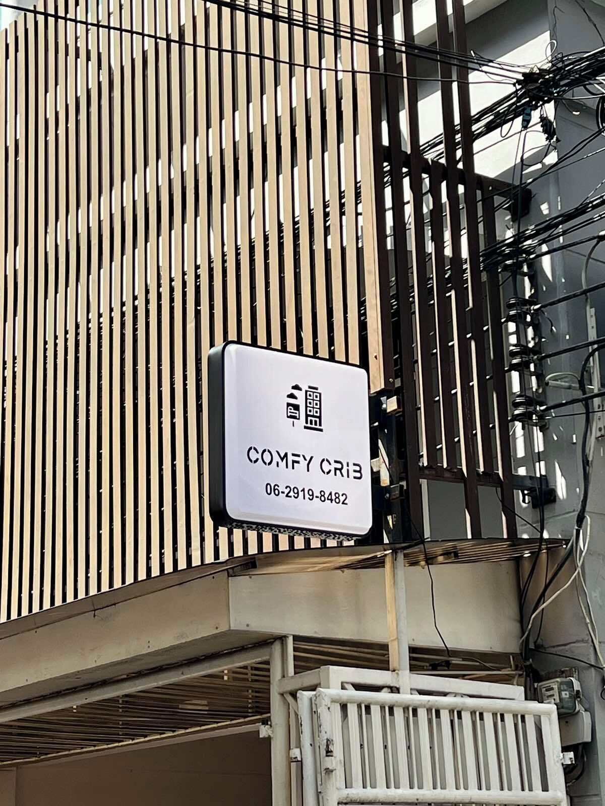 Une enseigne portant l’inscription « COMFY CRIB » et un numéro de téléphone, le « 06-2919-8482 », est fixée sur la façade d’un immeuble.