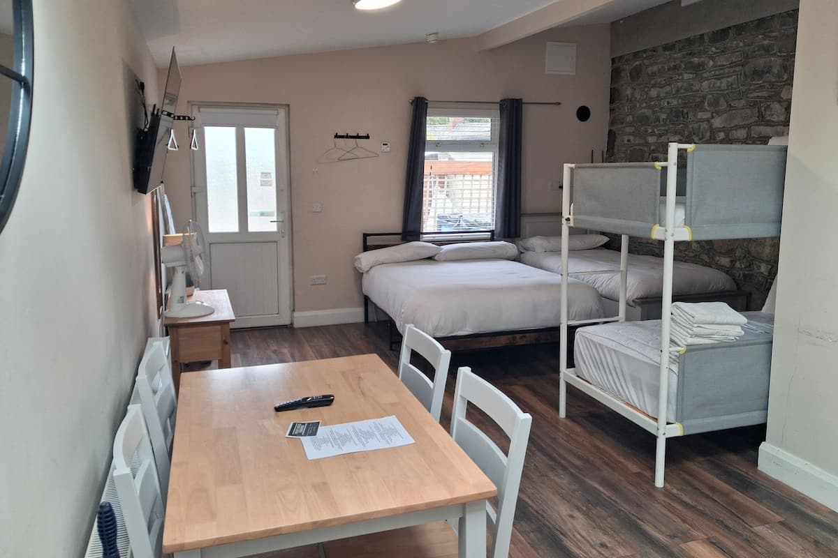 A compact room with a bunk bed, a single bed, a table with a remote control, and a window with curtains.