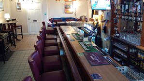A bar area with a long counter, multiple seating options, and a television screen displaying content. - Mattys Pub & Apartments (Muine Bheag)