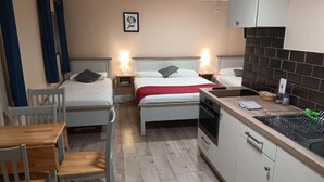 A compact hotel room with two single beds, a small kitchenette, a dining table with chairs, and a wooden floor. - Mattys Pub & Apartments (Muine Bheag)