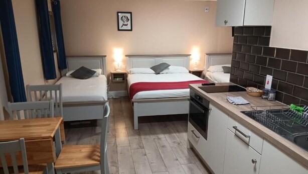 A compact hotel room with two single beds, a small kitchenette, a dining table with chairs, and a wooden floor. - Mattys Pub & Apartments (Muine Bheag)