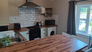 A compact kitchen with a wooden countertop, a microwave, a stove, and a built-in washing machine. - Mattys Pub & Apartments (Muine Bheag)
