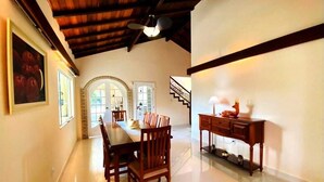 Uma sala de jantar com uma mesa e cadeiras de madeira, uma escada e uma escrivaninha com abajur.