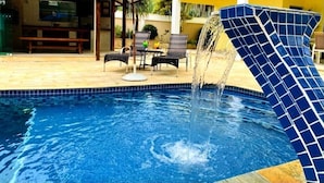 Piscina com fonte, área de estar externa e varanda coberta.