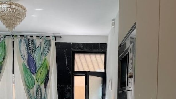 Een moderne woonkamer met een bank, een eettafel met stoelen, een keukenhoek en een groot raam met gordijnen.