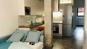 Een kleine kamer met een bed, een kitchenette en een badkamer.