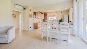 Uma sala de estar ampla com mesa e cadeiras, uma cozinha com armários de madeira e uma janela grande que oferece luz natural.