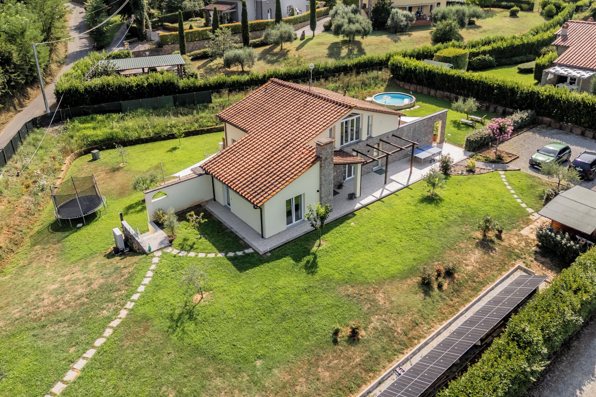 A modern two-story house with a tiled roof, a swimming pool, and a solar panel array.