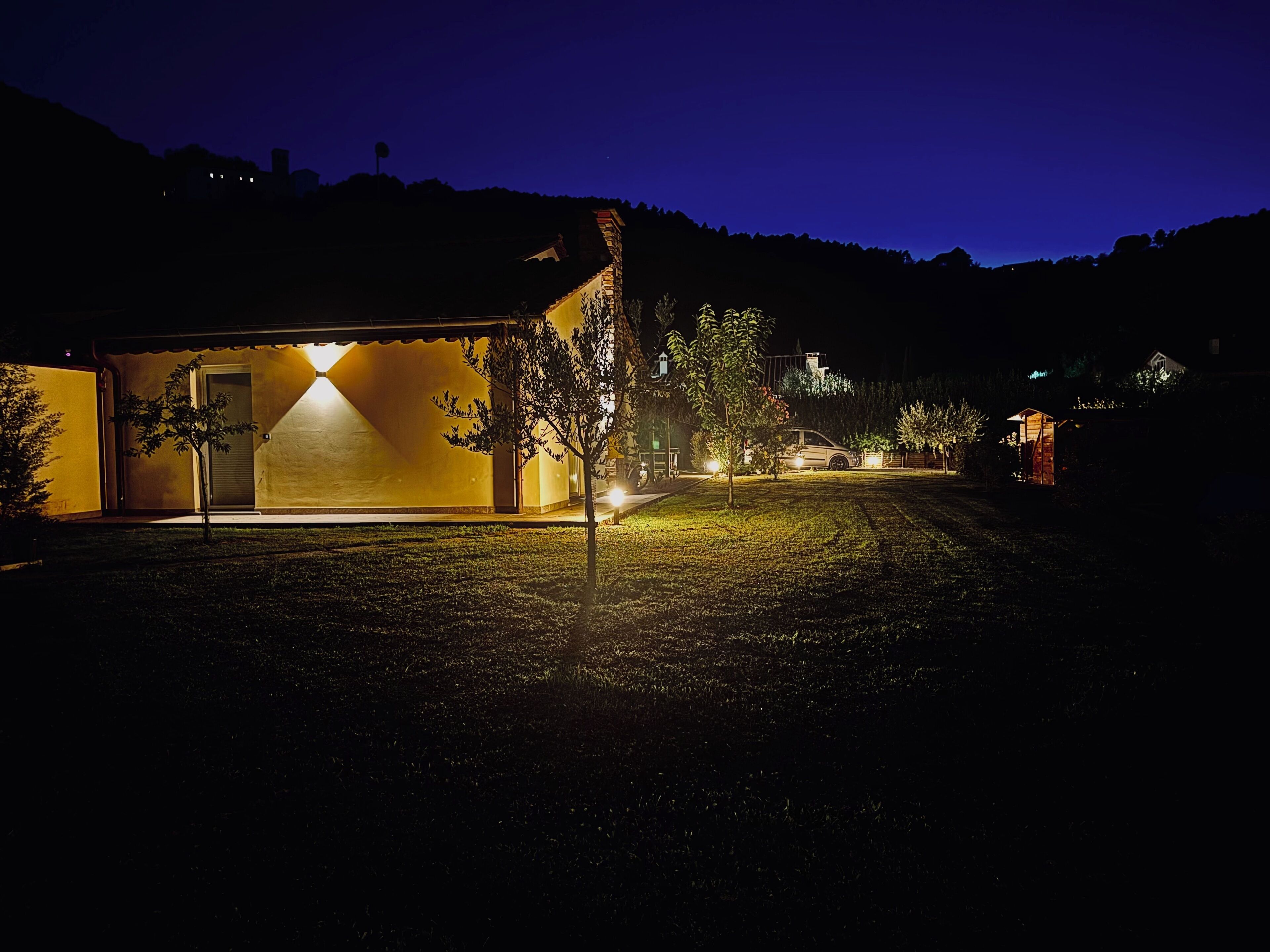 Ein Wohnhaus bei Nacht mit gut beleuchteter Garage und Auffahrt zu einem parkenden Auto.