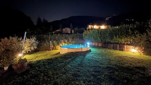 En trädgård med en pool, omgiven av ett staket och upplyst av trädgårdsbelysning.