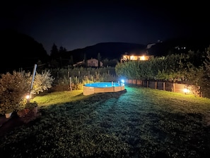 Een achtertuin met een zwembad, omgeven door een hek en verlicht met tuinverlichting.