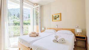 Quarto de hotel com duas camas, varanda, um quadro e mesa de cabeceira com abajur.