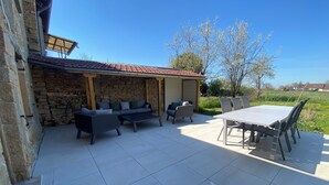 An outdoor patio with a stone wall, a covered seating area, and a dining table. - Village house (9 pers), ideal for families, in the heart of the Jura mountains (Cesancey)