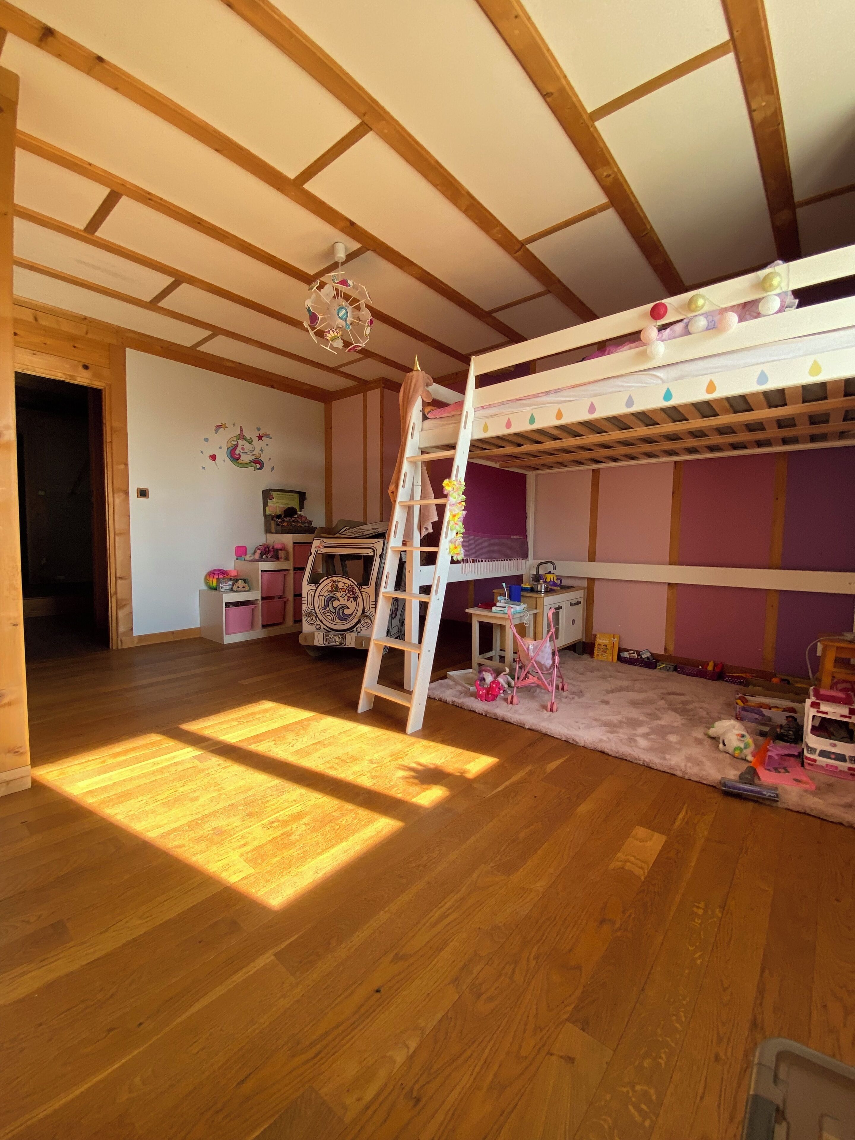 Une chambre avec un lit superposé, des poutres en bois, une échelle, un bureau et divers jouets.