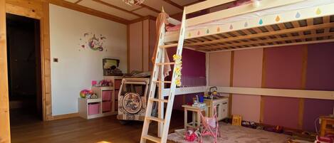 Une chambre avec un lit superposé, des poutres en bois, une échelle, un bureau et divers jouets.