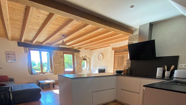 A spacious kitchen with a wooden ceiling, a stone wall, and a large window. - Village house (9 pers), ideal for families, in the heart of the Jura mountains (Cesancey)