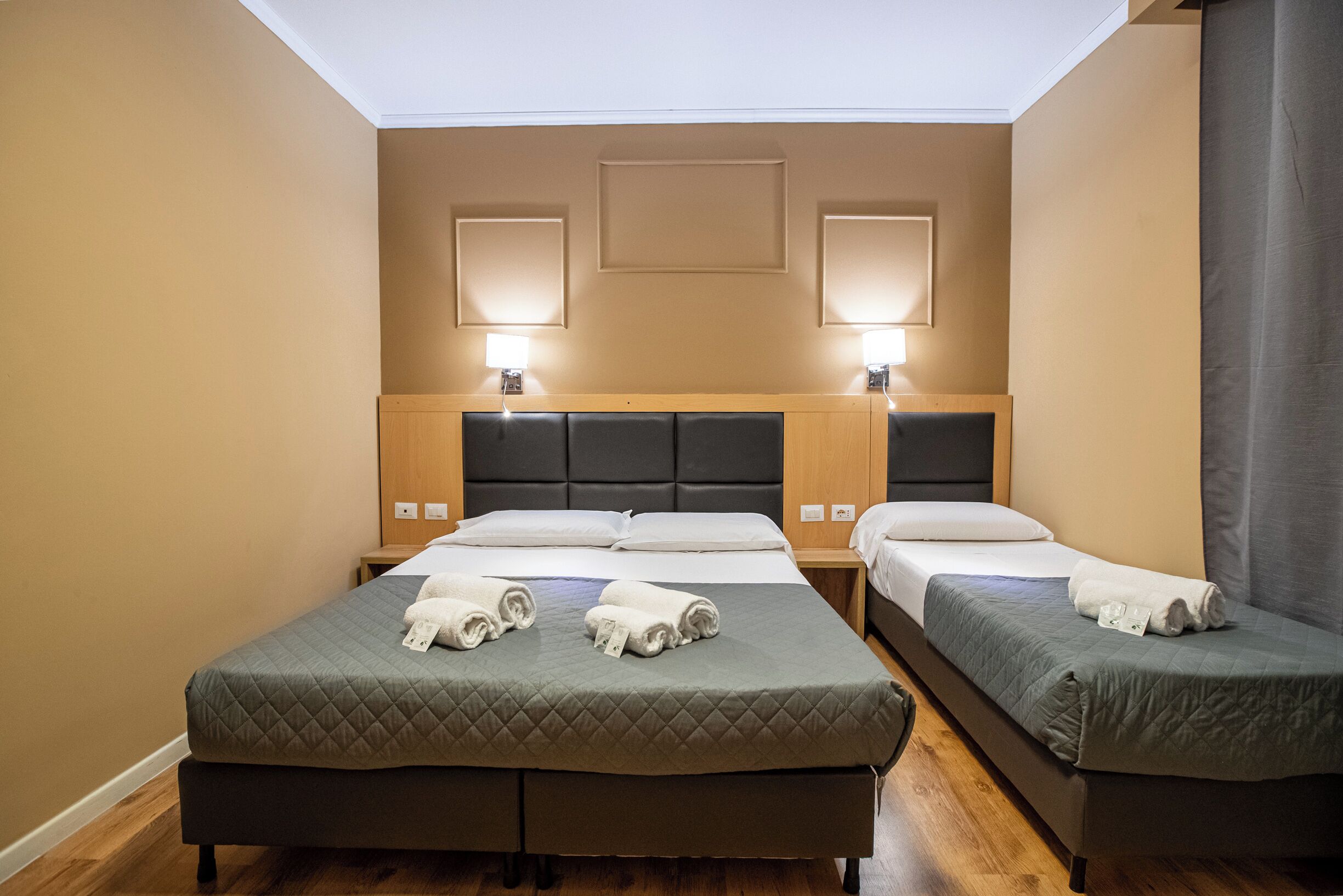 Habitación de hotel con dos camas, cabecera de madera, lámparas de noche y vista al cielo a través de la ventana.