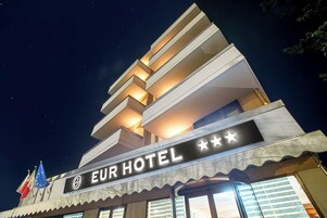 Un hotel llamado "EUR HOTEL" con un diseño arquitectónico moderno, que cuenta con varios balcones y un llamativo letrero con estrellas.