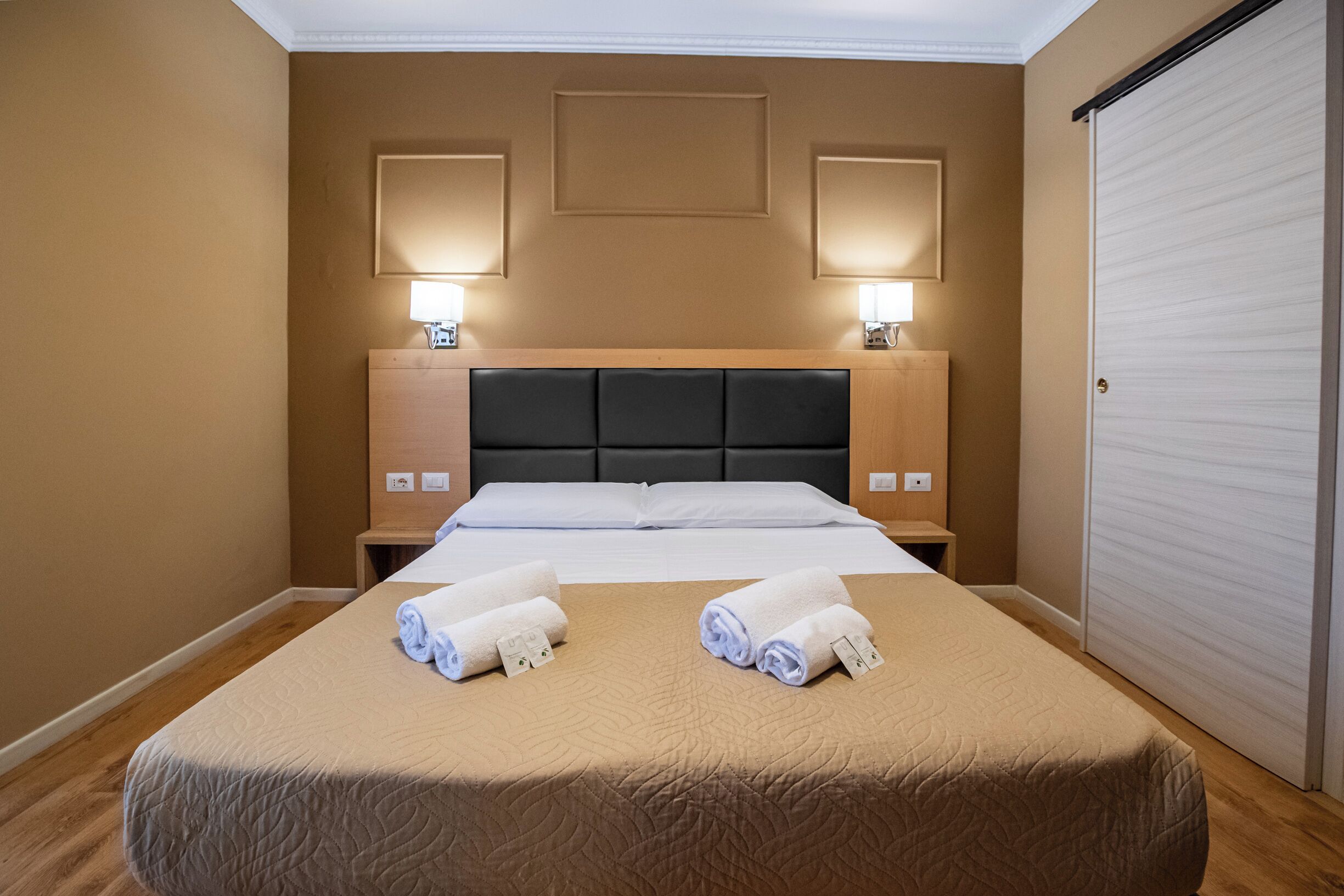 A hotel room with a large bed, two bedside tables, and a wardrobe.