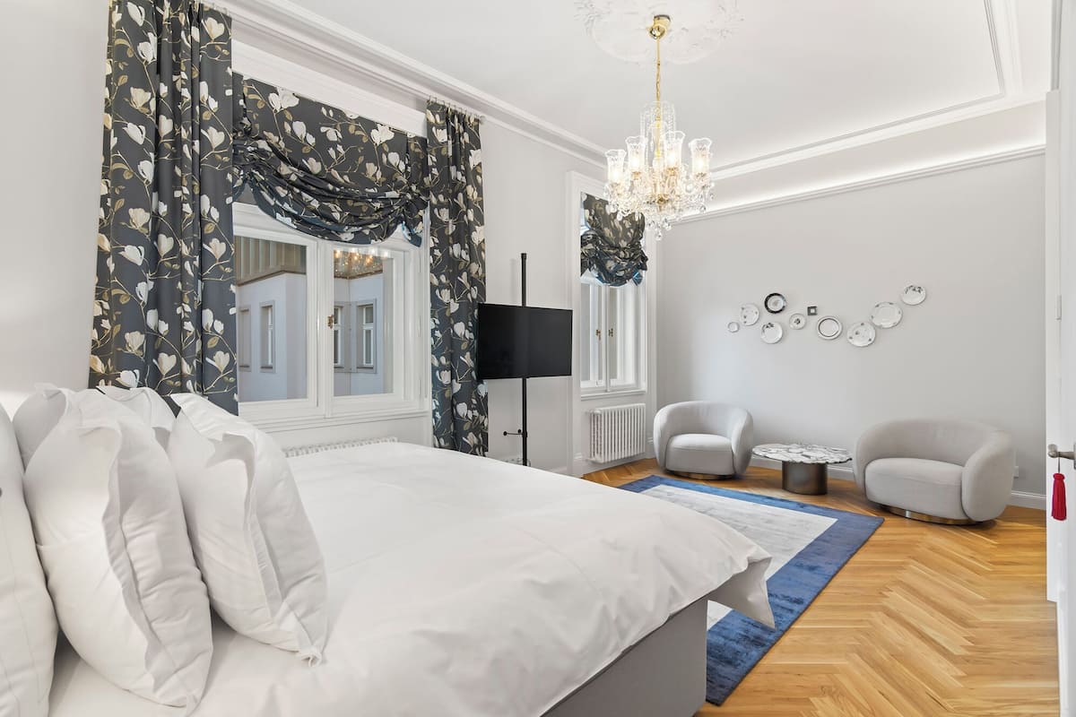 Une chambre à coucher avec un grand lit, un lustre, un bureau, deux chaises et un mur décoré d’assiettes.