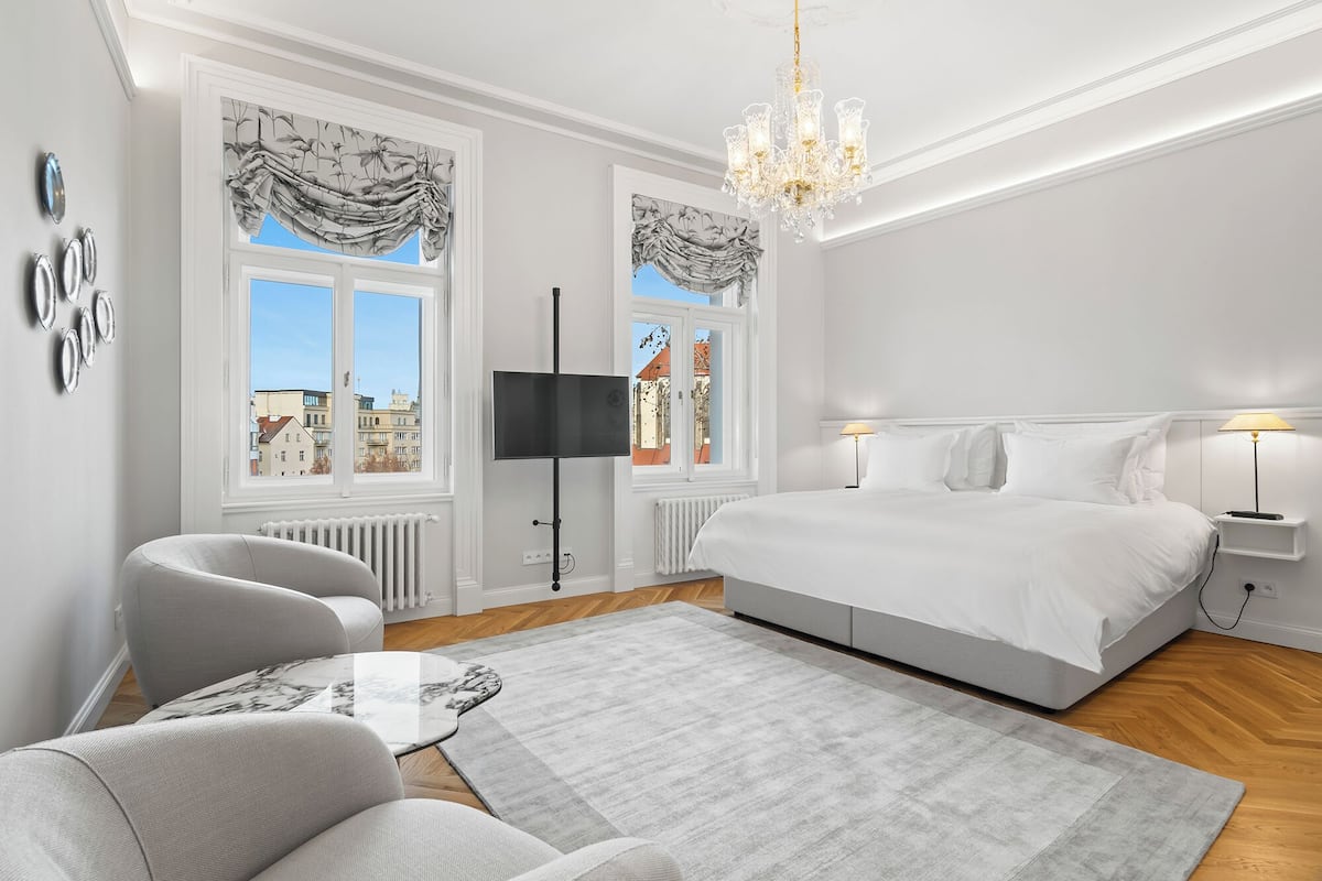 Une chambre moderne avec un grand lit, un lustre et une vue sur les immeubles par les fenêtres.