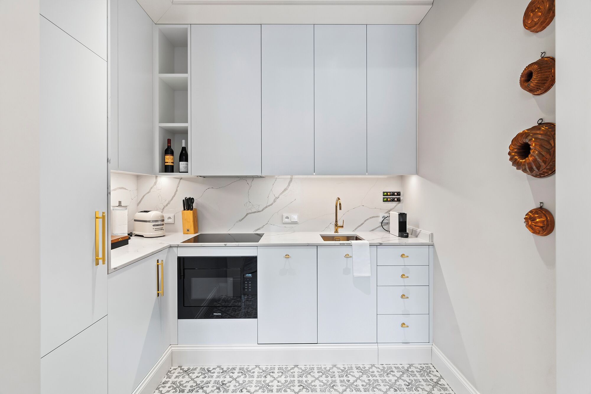 A modern kitchen with white cabinets, a built-in oven, a microwave, and a sink.