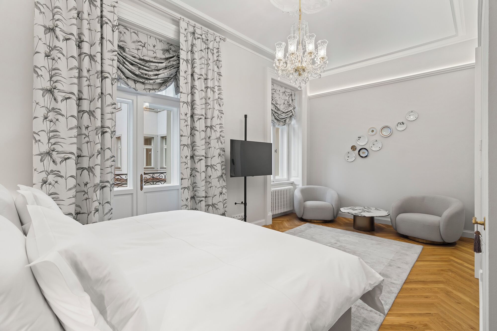 A modern bedroom with a large bed, a flat-screen TV, a chandelier, and a wall of decorative plates.