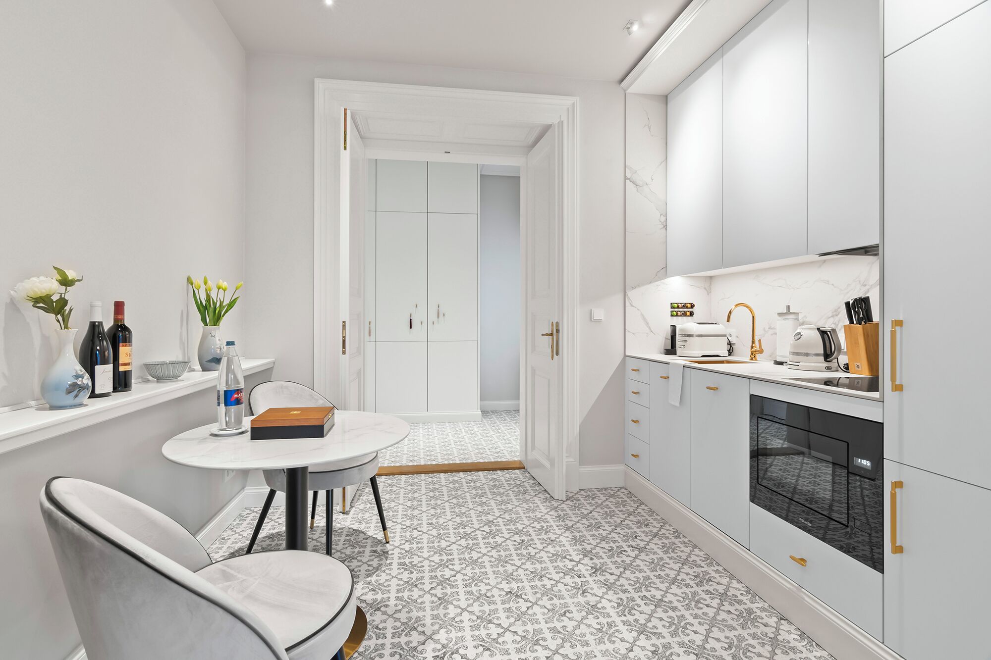 A modern kitchen with white cabinetry, a built-in oven, and a dining area with a round table and two chairs.
