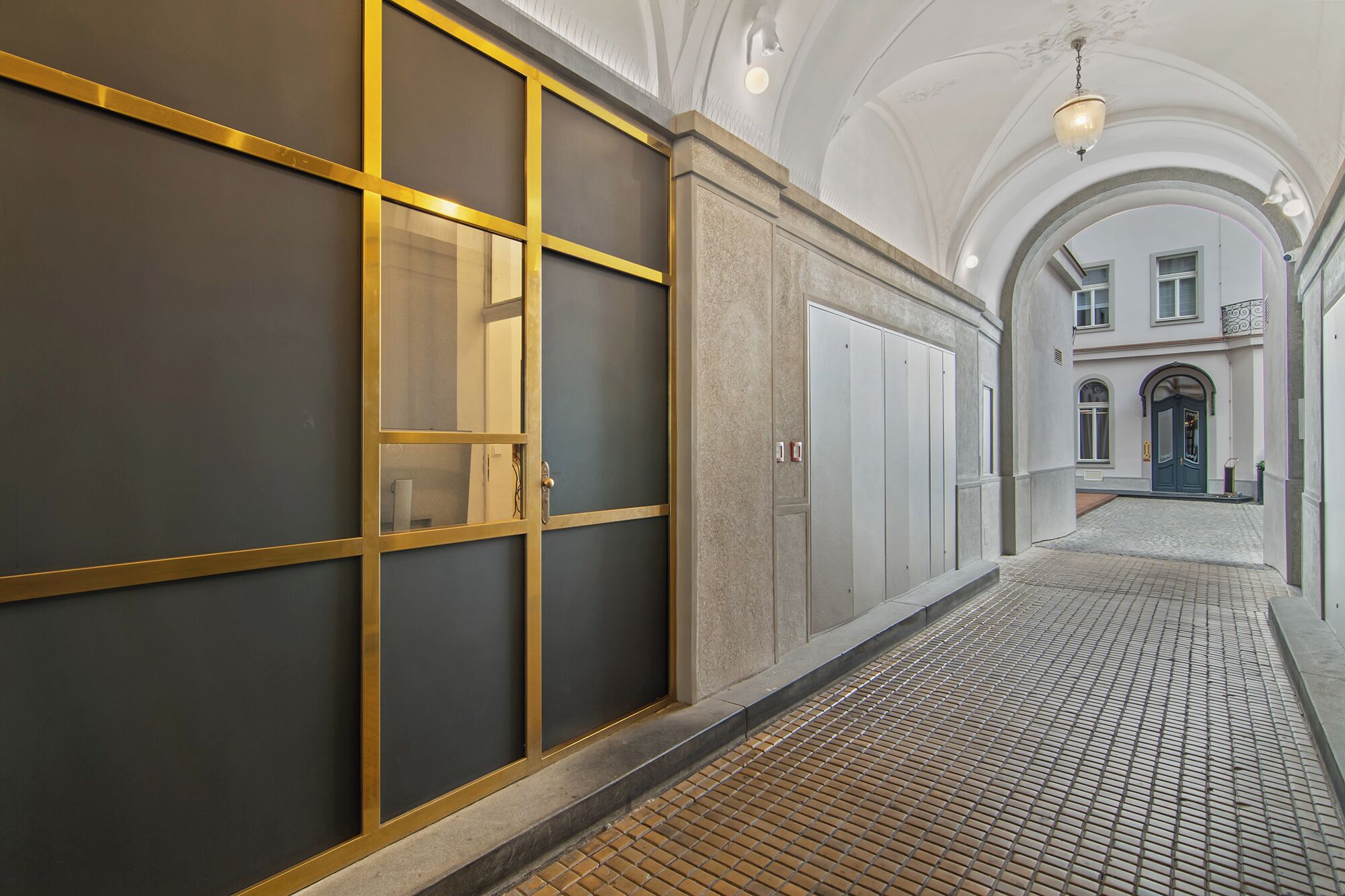 A corridor with a tiled floor, a large window with a golden frame, and a door with a keypad lock.