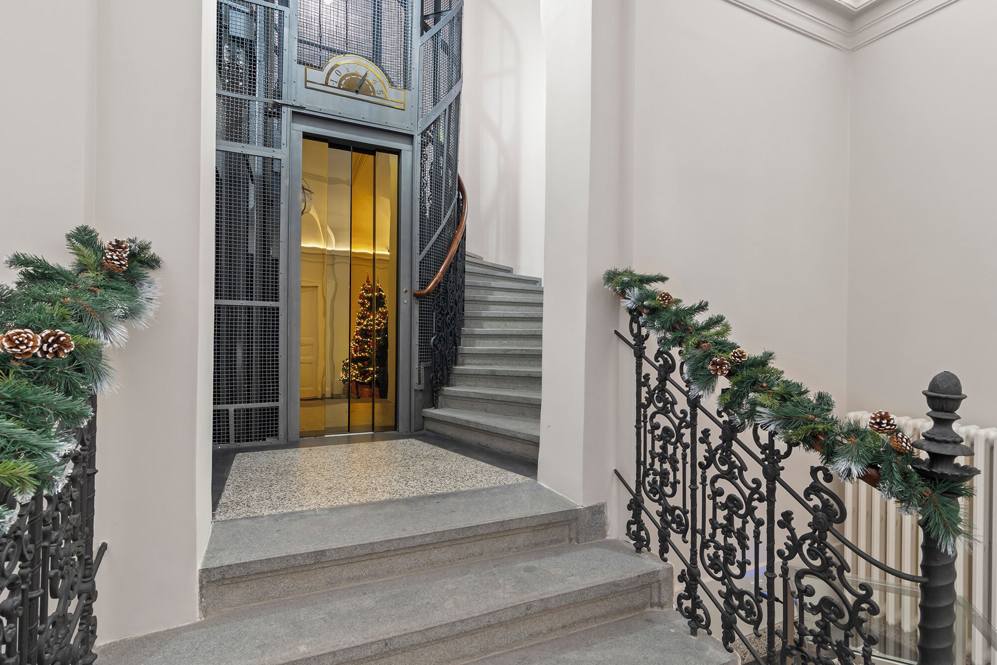 A staircase with a metal railing, a glass door with a golden frame, and a Christmas tree inside.