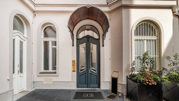 A building entrance with a dark blue door, a small black mat with the number 33, and a potted plant to the right. - Vodičkova Luxury Suites (Prague)