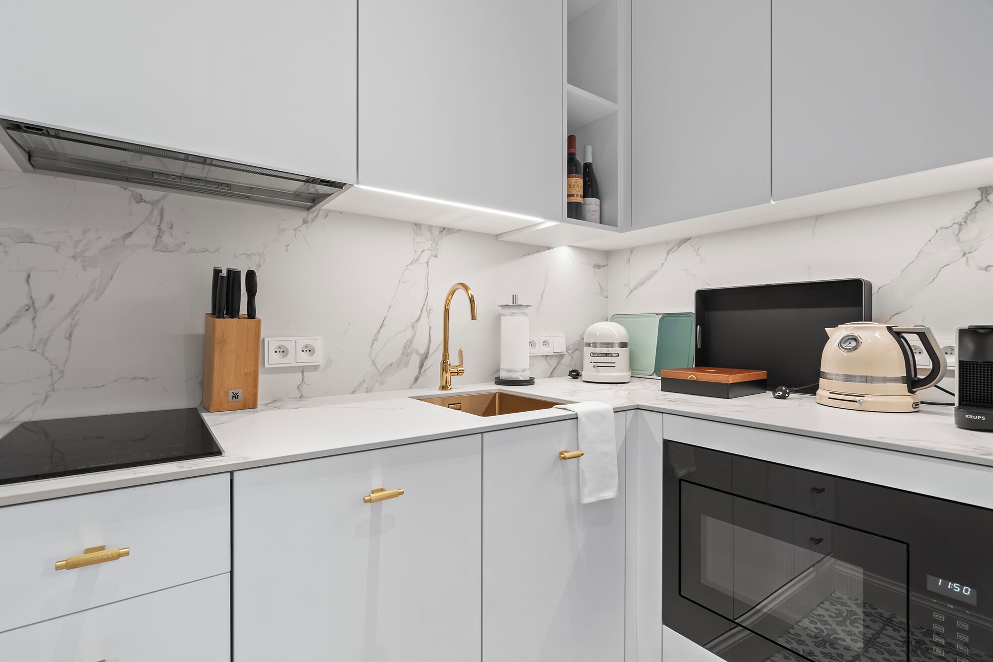 Een moderne keuken met een witte marmeren spatwand, een ingebouwde oven en een koffieapparaat.