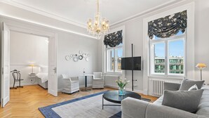 A modern living room with a chandelier, a flat-screen TV, and a large window with curtains. - Vodičkova Luxury Suites (Prague)