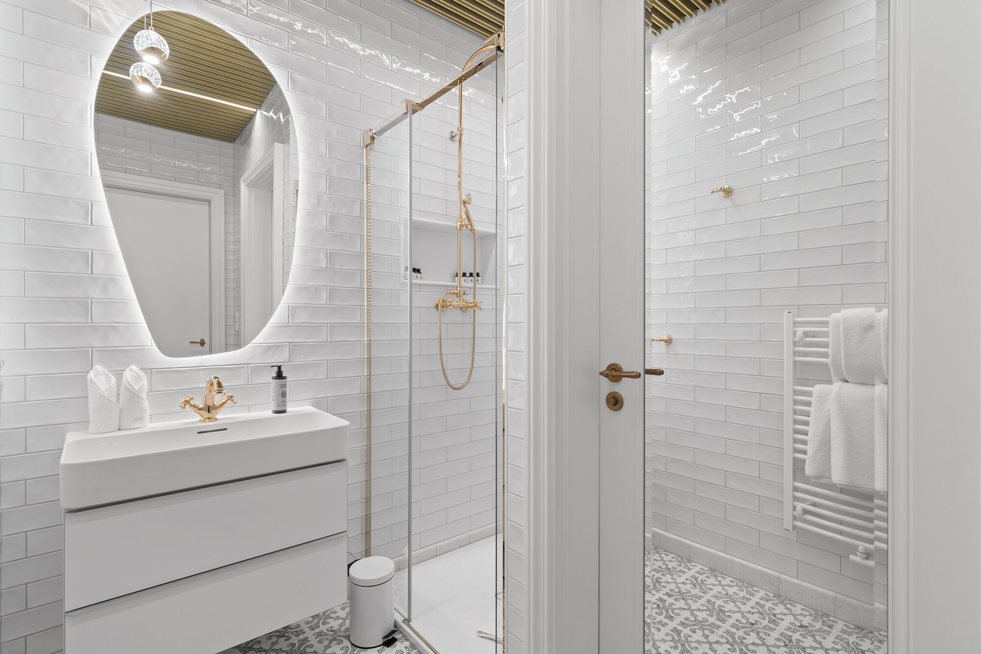 Un baño moderno con azulejos blancos tipo metro, un cabezal de ducha dorado y un tocador blanco con espejo.