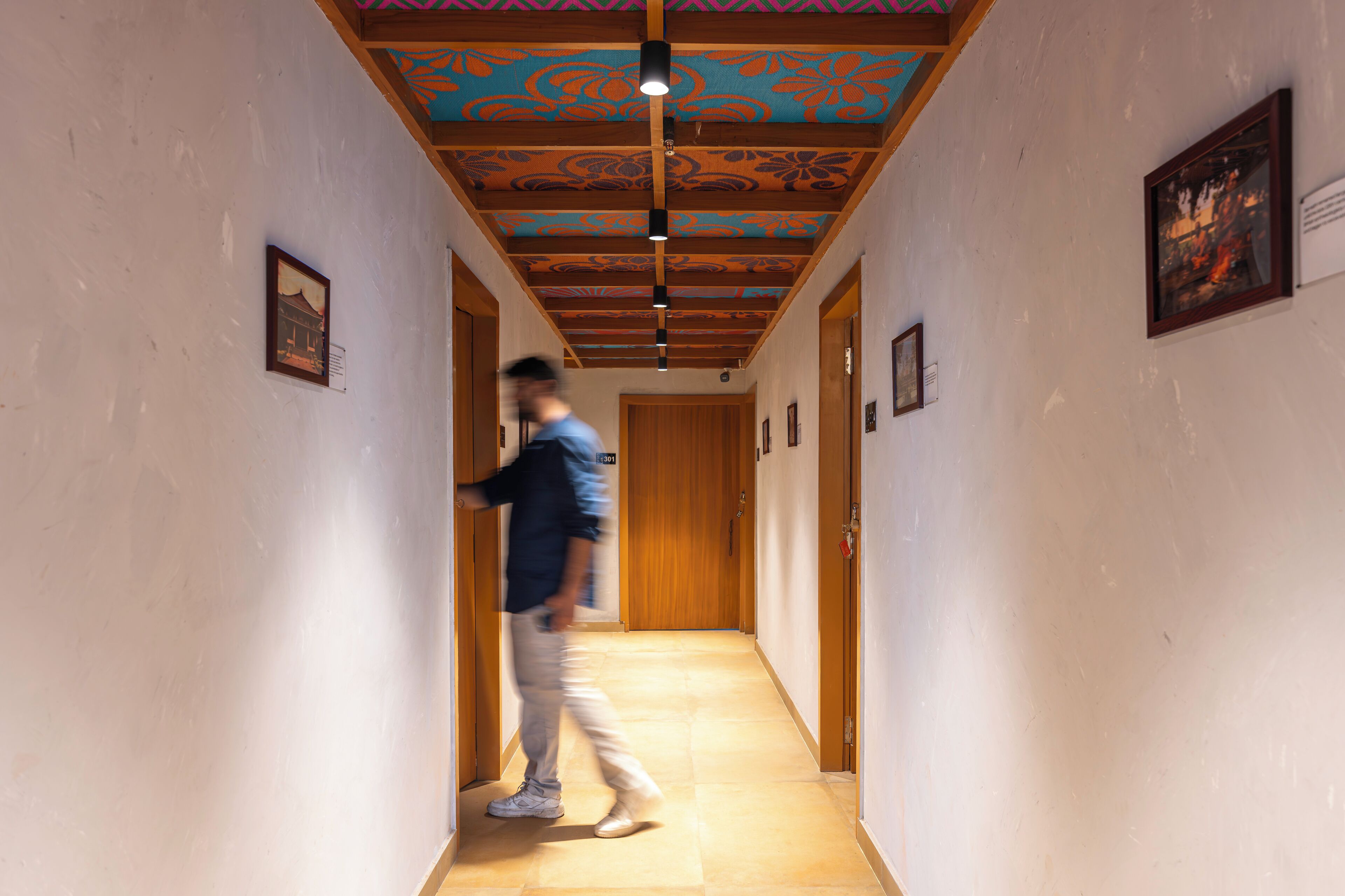 A hallway with a wooden door at the end, a patterned ceiling, and framed pictures on the walls.