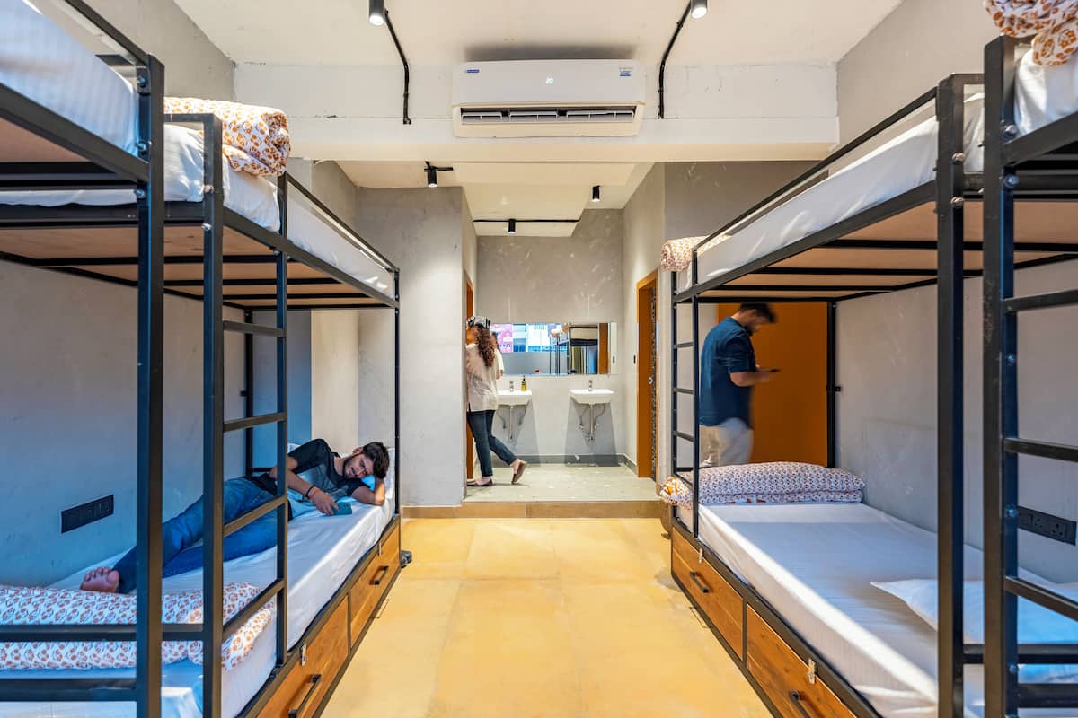 Une chambre de dortoir avec des lits superposés, une salle de bain avec des lavabos et un couloir menant à une autre pièce.