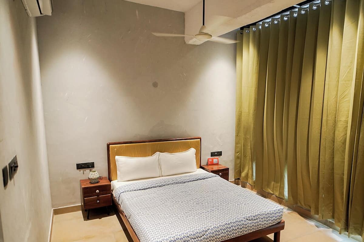 Une chambre à coucher avec un lit, des tables de chevet, un ventilateur de plafond et une fenêtre avec des rideaux.