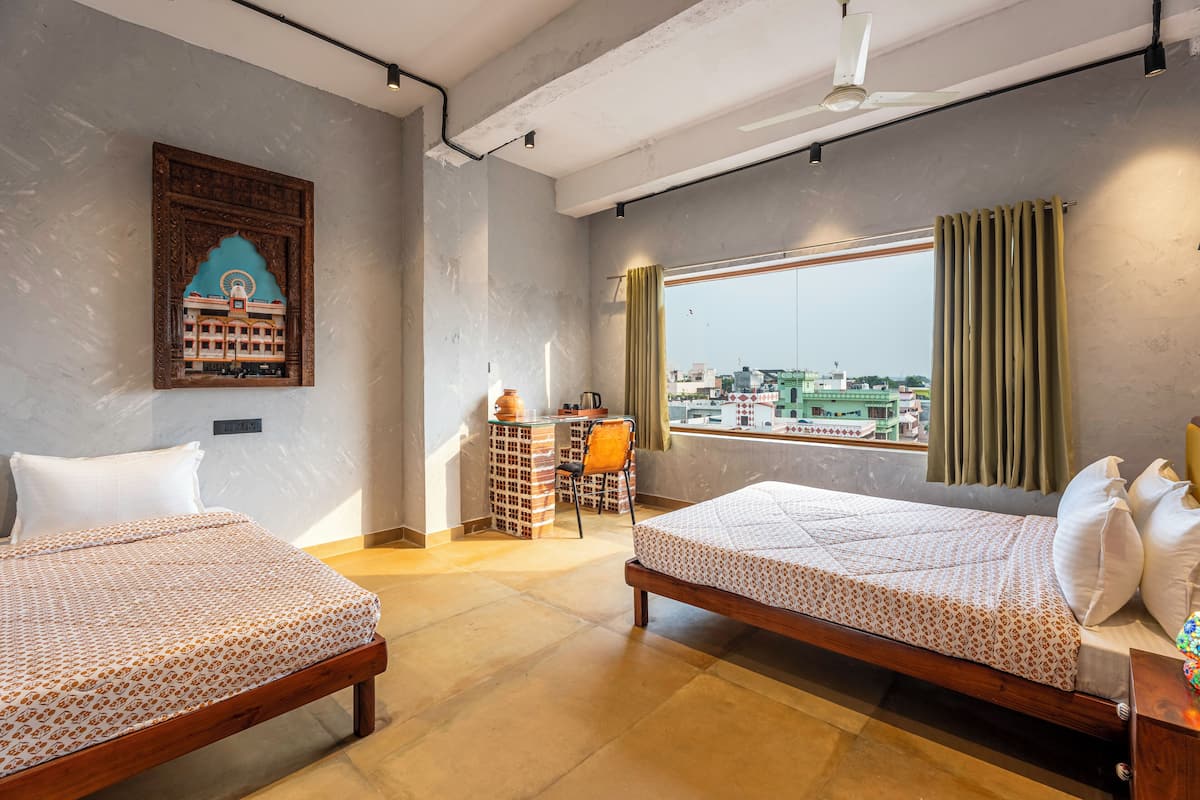 Une chambre d’hôtel avec deux lits, une fenêtre avec des rideaux, un élément décoratif mural et une vue sur la ville.