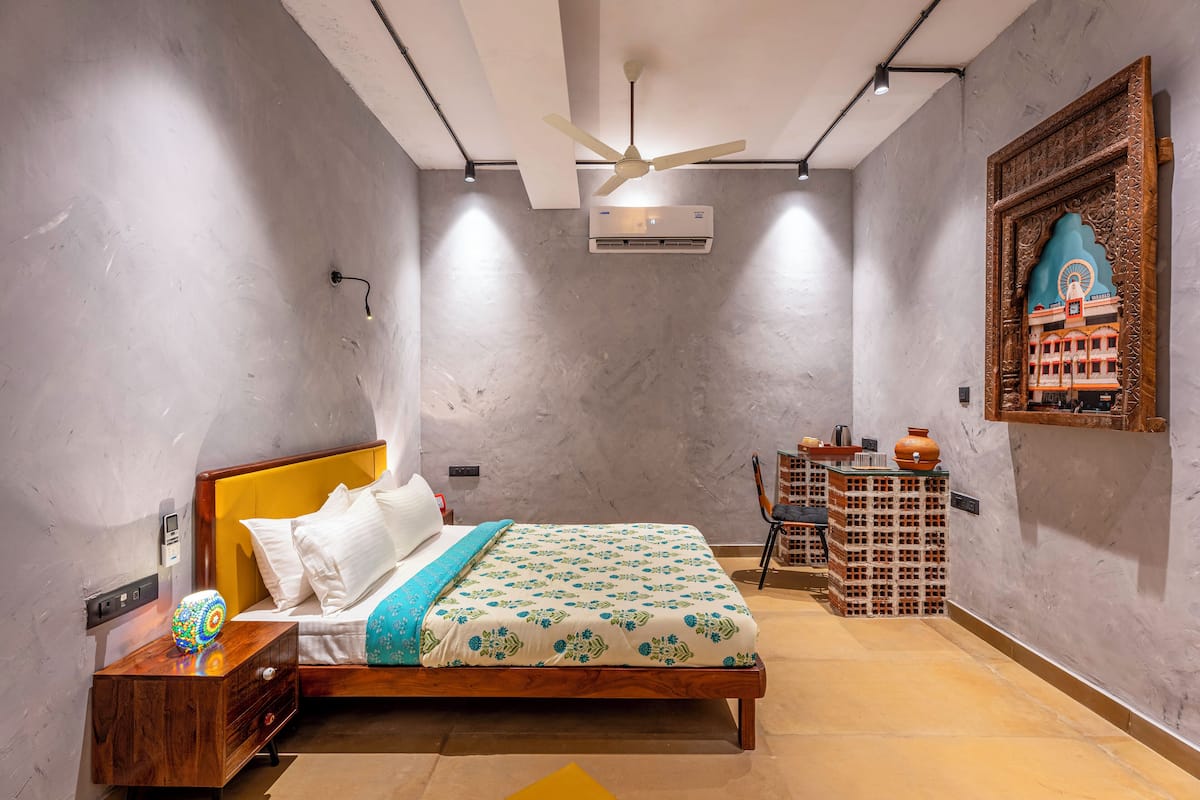 Une chambre à coucher comprenant un lit, une table de chevet, une commode, un ventilateur de plafond, un appareil de climatisation et un élément décoratif mural.