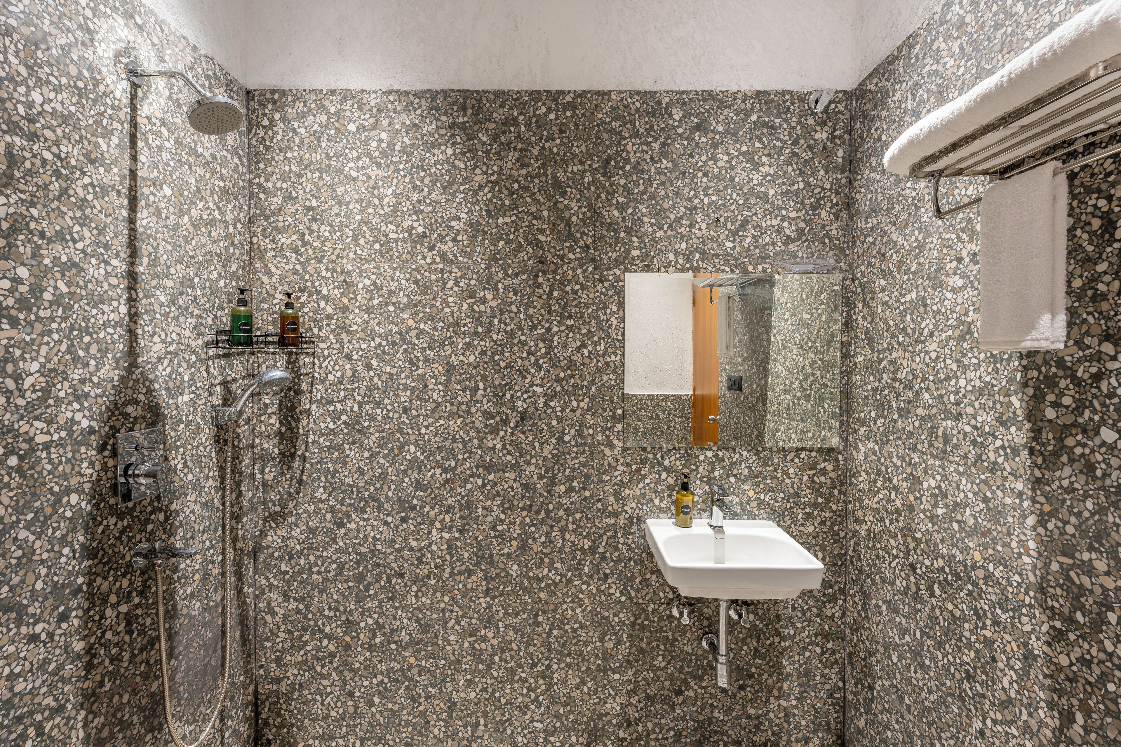 A bathroom with a pebble-textured wall, a shower, a sink, and a mirror.