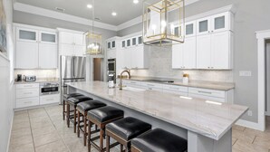 Una cocina moderna con armarios blancos, una isla grande de mármol y taburetes de bar.