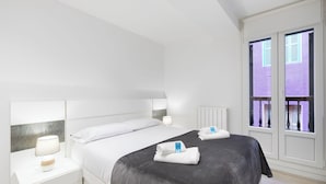 A modern bedroom with a large bed, bedside tables with lamps, and a window with a view of a building.