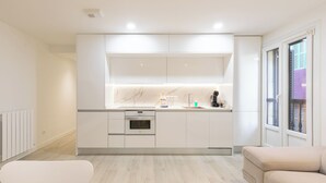 A modern kitchen with white cabinetry, a built-in oven, and a window with a view of a purple building.