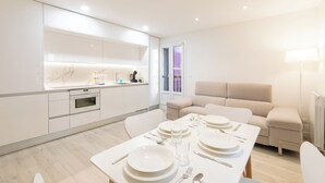 A modern kitchen with white cabinets, a marble backsplash, and a dining area set with white tableware.