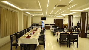 A restaurant with long tables, chairs, and a ceiling fan. - Hotel Singhnature (Khandwa)