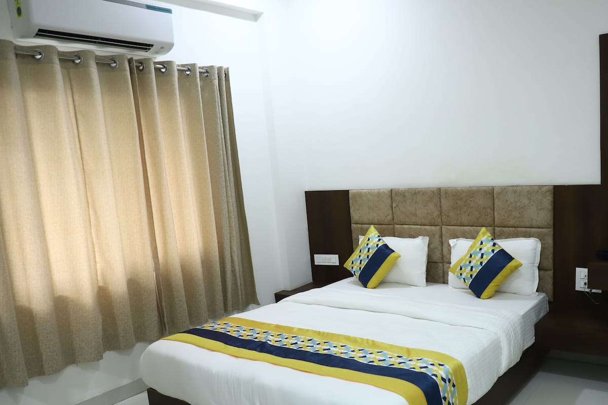 A hotel room with a bed, curtains, and a wall-mounted air conditioner.